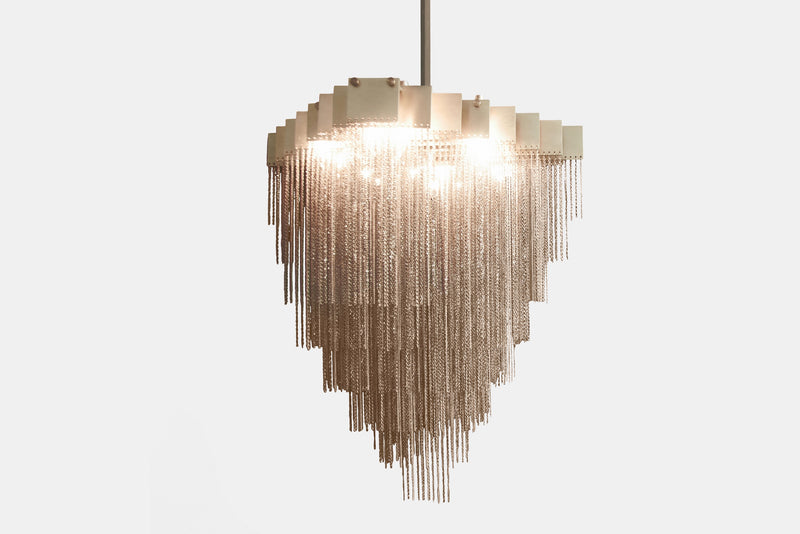 A made to order chandelier that moves with glamorous intrigue, the KELLY Chandelier’s metallic chain cascades through its various layers to create a glisten reflective effect. The epitome of high end lighting, this bespoke chandelier provides a handmade designer lighting solution for luxury interior design.