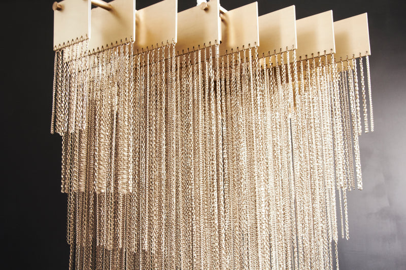 A luxury chandelier that moves with glamorous intrigue, the KELLY Chandelier’s metallic chain cascades through its various layers to create a glisten reflective effect. This contemporary light design creates a bold synergy of cold metal with warm light, a perfect addition to modern interior design.